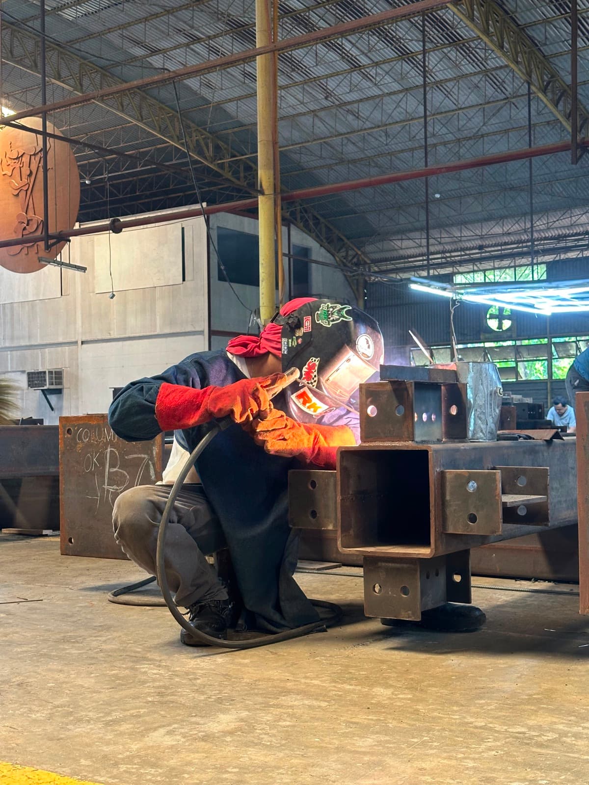 Prior plant work — welder on a structural steel column marked COLUMN OK, San Simon (not a Calma.Basic product)